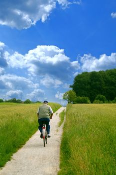 A senior person cycling on a small path.