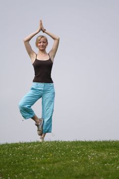 A young handsome woman doing gymnastics on a meadow.