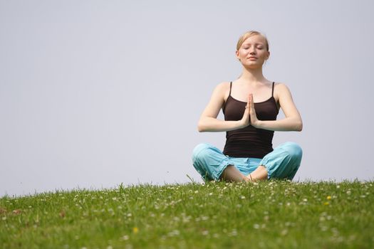 A young handsome woman doing gymnastics on a meadow.