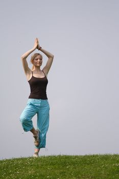 A young handsome woman doing gymnastics on a meadow.