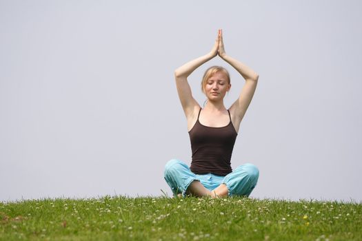 A young handsome woman doing yoga on a meadow.