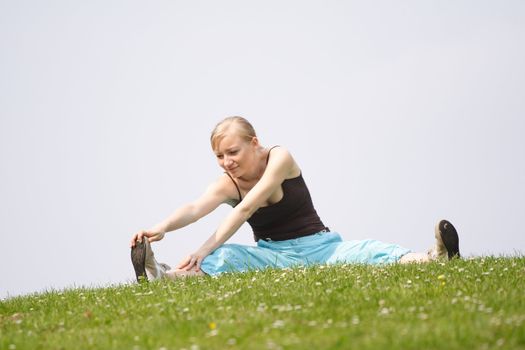 A young handsome woman doing gymnastics on a meadow.