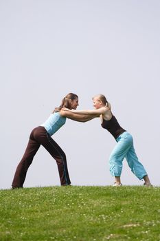 Two handsome young women doing gymnastics on a green meadow. ** Note: Slight blurriness, best at smaller sizes.