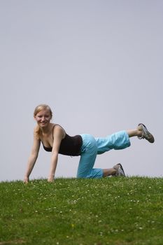 A young handsome woman doing gymnastics on a meadow.