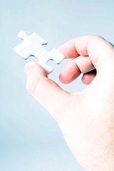 A person holding a white piece of a puzzle in his hand. All on light blue background.