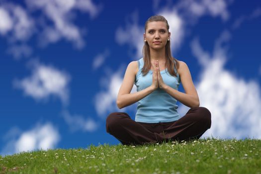 A young handsome woman doing gymnastics on a meadow infront of a bright blue sky.