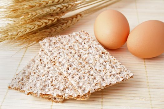 Some crispbread lying next to grain and some eggs.