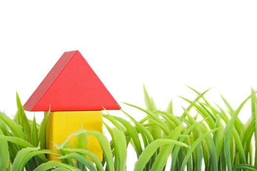 A stylized house out of blocks between blades of grass. All isolated on white background.