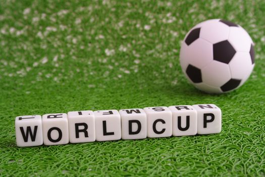 A simple soccer ball lying on green meadow. The term worldcup on white dices lying next to it.