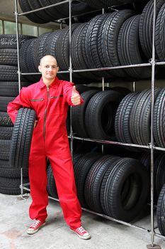 An optimistic mechanist standing next to a rack full of tires.