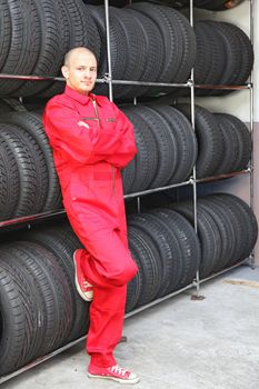 An optimistic mechanist standing next to a rack full of tires having a short break.