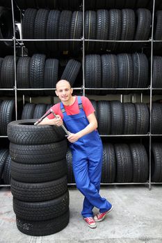 An optimistic mechanic standing in front of a rack full of tires.