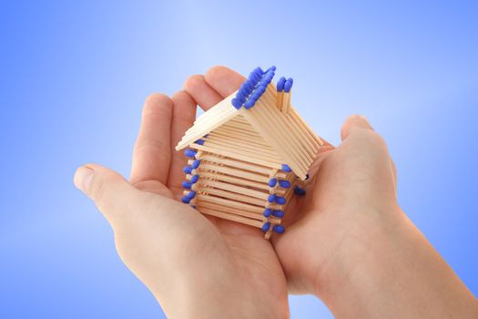 A human hand protecting a stylized house out of matchsticks. All isolated on light blue background.