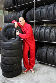 An optimistic mechanist standing next to pile of tires.