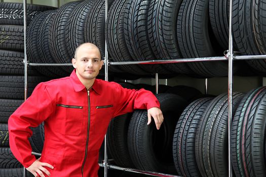 An aspiring worker in a workshop, standing next to a to a rack full of tires.