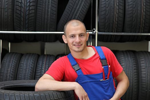 An optimistic mechanic standing in front of a rack full of tires.