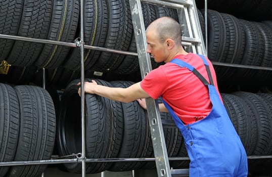 A motivated worker in a tire workshop standing on a ladder and checking the stock.