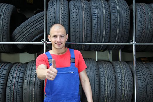 An optimistic mechanist standing in front of a rack full of tires.