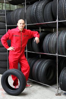 An optimistic mechanist standing next to a rack full of tires.