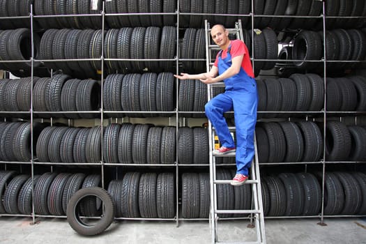 A smiling mechanic in a garage presenting the range of goods.