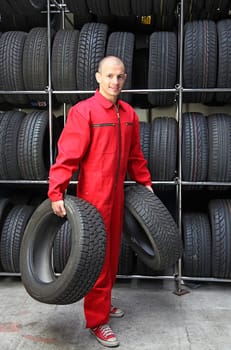 A motivated worker in a tire workshop carrying two tires.