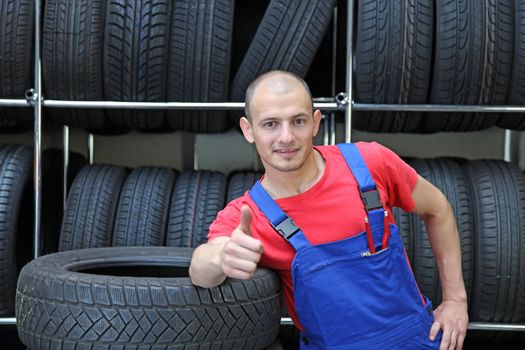 An optimistic mechanist standing in front of a rack full of tires.