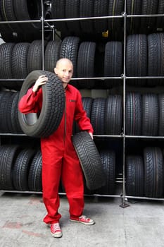 A motivated worker in a tire workshop carrying two tires.