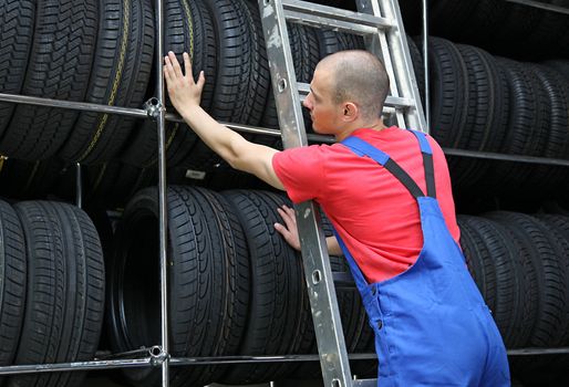 A motivated worker in a tire workshop standing on a ladder and checking the stock.