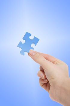 A person holding a blue piece of a puzzle in his hand. All on bright blue background.