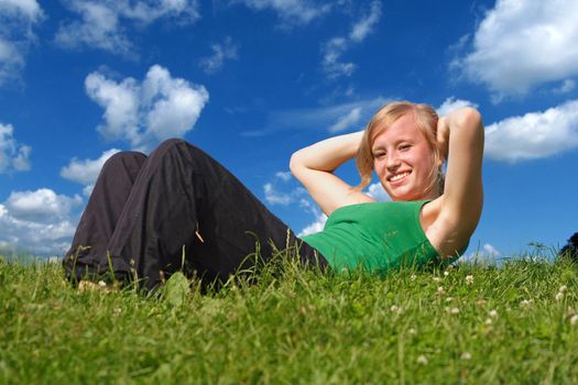 On a summery day a sporty girl is doing exercises outside.