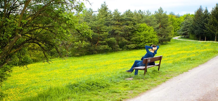 male resting on the bench on the field of dandelions