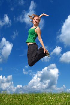 A young attractive woman jumping on a meadow in front of a bright blue sky.