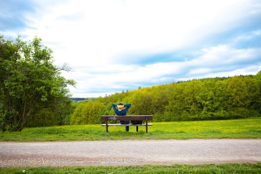 male resting on the bench on the field of dandelions