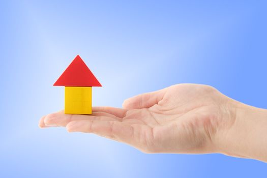 A human hand holding a stylized house out of colored blocks. All isolated on light blue background.