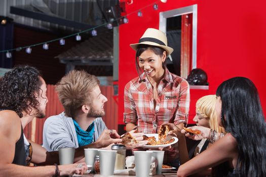 Smiling Asian woman sharing pizza slices with friends at food truck