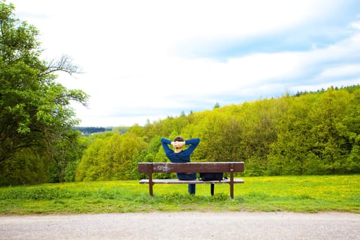 male resting on the bench on the field of dandelions