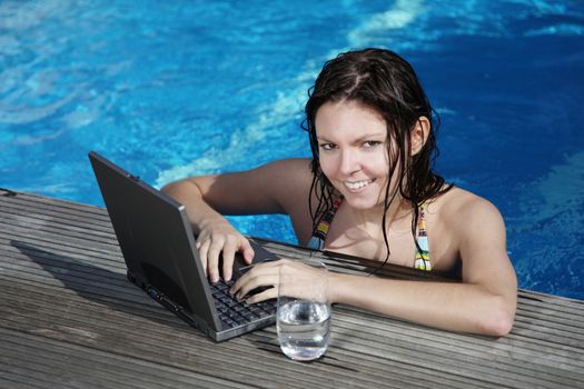 A very attractive young woman refreshing in a swimming pool and surfing the internet on her notebook computer.