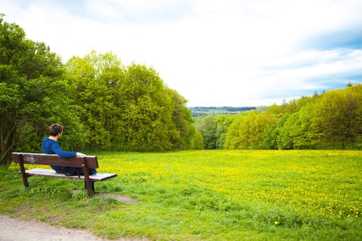 male resting on the bench on the field of dandelions