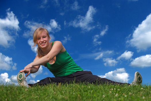 On a summery day a sporty girl is doing exercises outside.