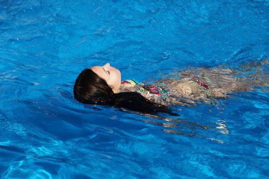 An attractive young woman swimming in a shiny blue pool.