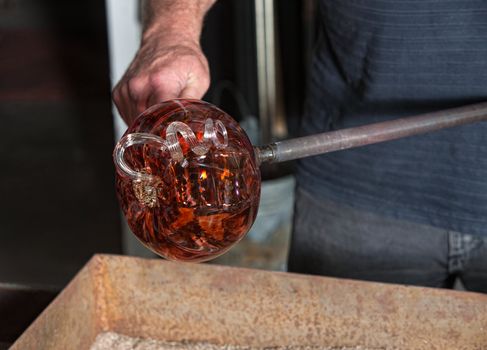 Worker holding fancy glass pumpkin vase with iron tool