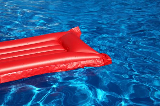 An inflatable red air mattress swimming in a shiny blue swimming pool.