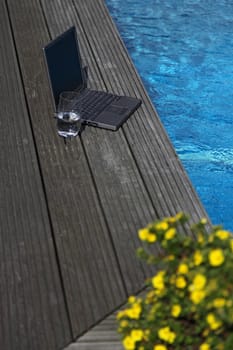 A notebook computer lying next to a swimming pool.