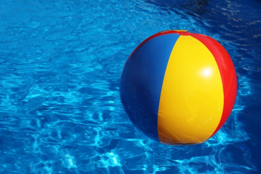 An inflatable colored plastic ball swimming in a shiny blue swimming pool.