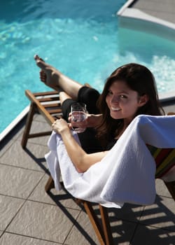 A very attractive young woman enjoying the sun while sitting in a deck chair next to a swimming pool.