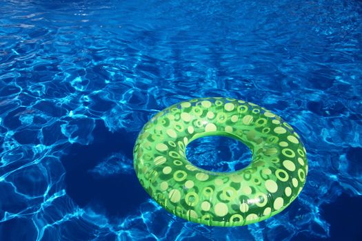 An inflatable green plastic ring swimming in a shiny blue swimming pool.