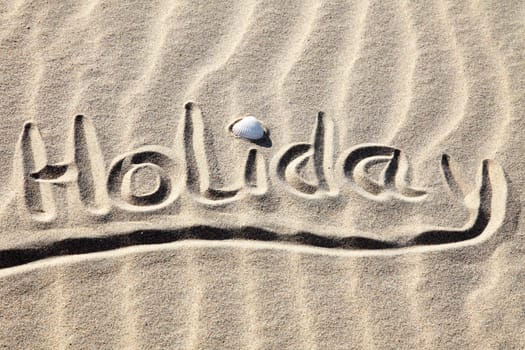 Holiday written in golden sand on a beach.