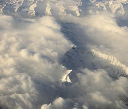 Aerial view of snowy mountains almost covered by clouds just before sunset
