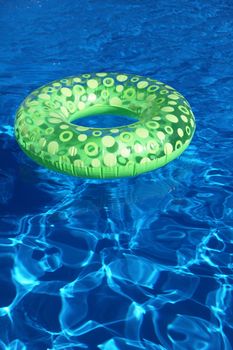 An inflatable green plastic ring swimming in a shiny blue swimming pool.