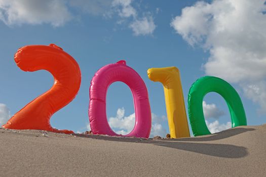 The year 2010 with inflatable numbers on the beach in front of a bright blue sky.